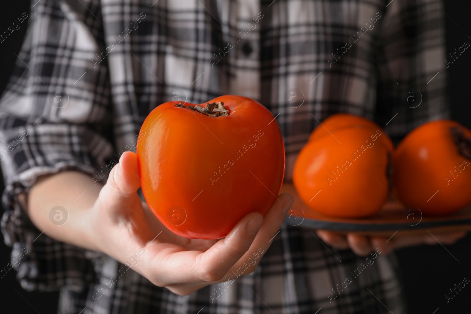 Photo of Woman holding delicious ripe juicy persimmons on black background, closeup