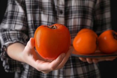 Photo of Woman holding delicious ripe juicy persimmons on black background, closeup