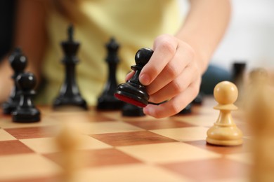 Photo of Little child playing chess, closeup of hand