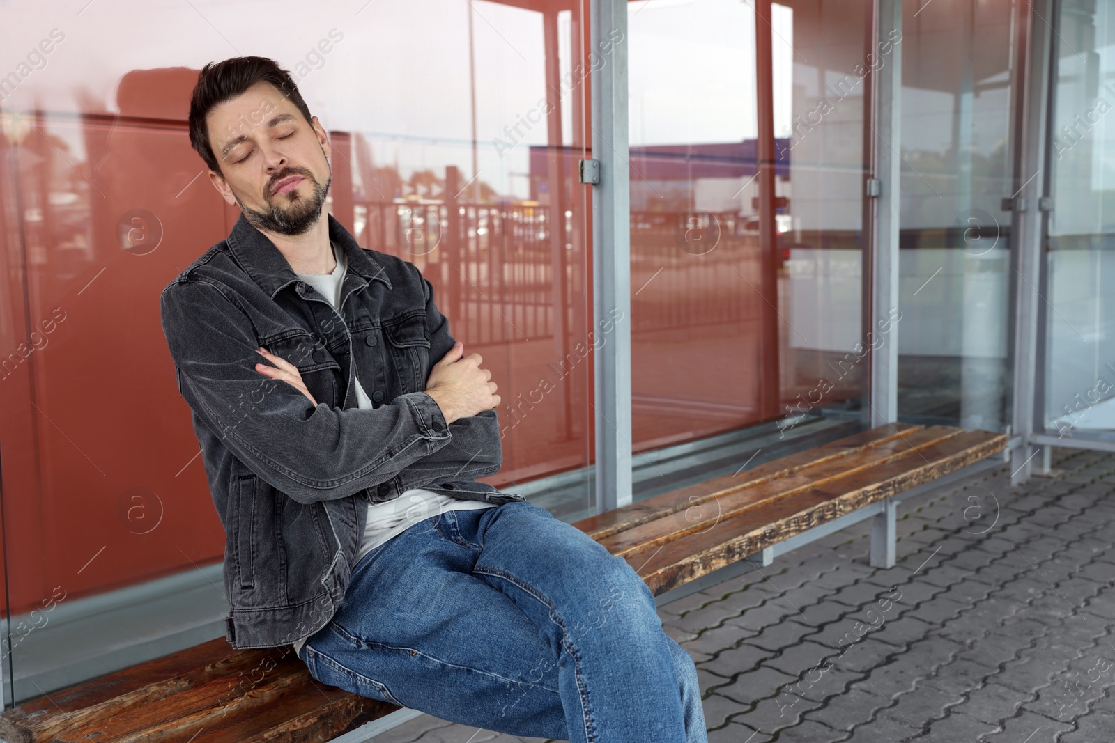 Photo of Tired man sleeping at public transport stop outdoors