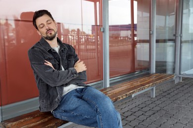 Tired man sleeping at public transport stop outdoors