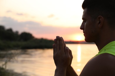 Photo of Man meditating near river at sunset. Space for text
