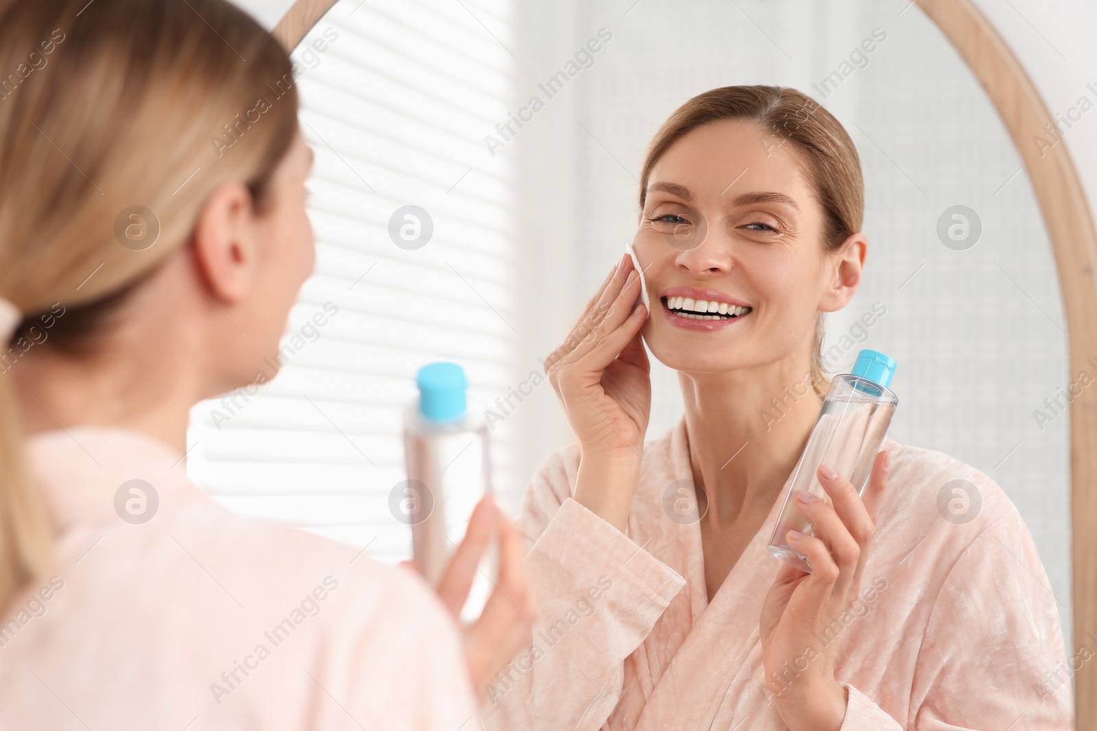 Photo of Beautiful woman removing makeup with cotton pad near mirror indoors