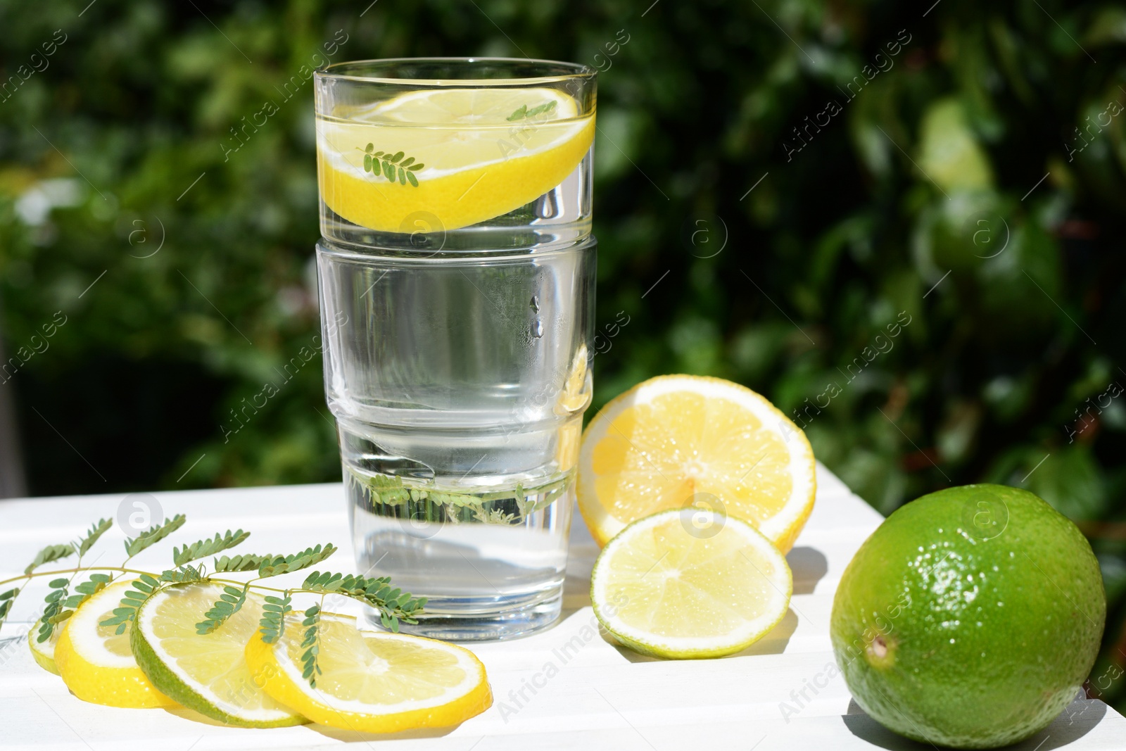 Photo of Delicious refreshing lemonade and pieces of citrus on white wooden table outdoors