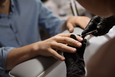 Photo of Professional manicurist cutting client's cuticle in beauty salon, closeup