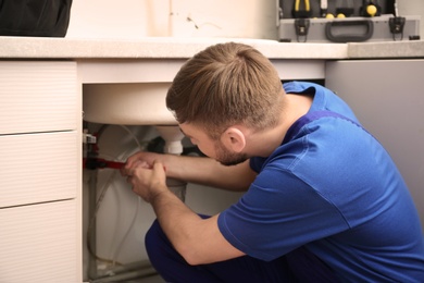 Photo of Professional plumber in uniform fixing kitchen sink