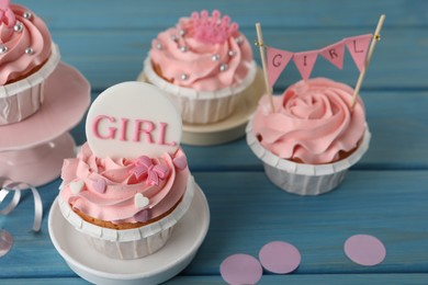 Photo of Delicious cupcakes with pink cream and toppers for baby shower on light blue wooden table