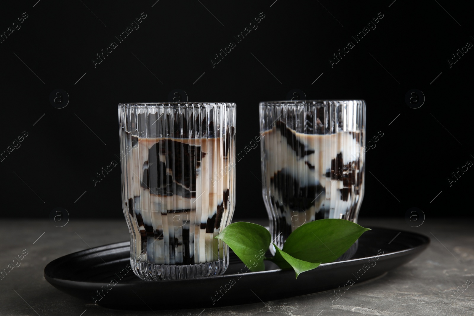 Photo of Glasses of milk with grass jelly and green leaves on grey table