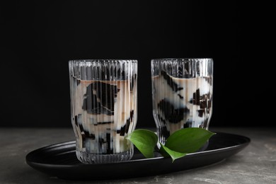 Photo of Glasses of milk with grass jelly and green leaves on grey table