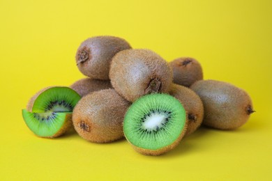 Heap of whole and cut fresh kiwis on yellow background