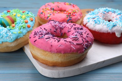 Photo of Sweet glazed donuts decorated with sprinkles on light blue wooden table. Tasty confectionery