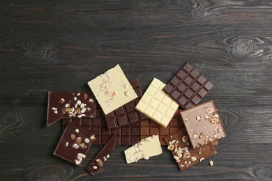 Different chocolate bars with nuts on wooden background, top view