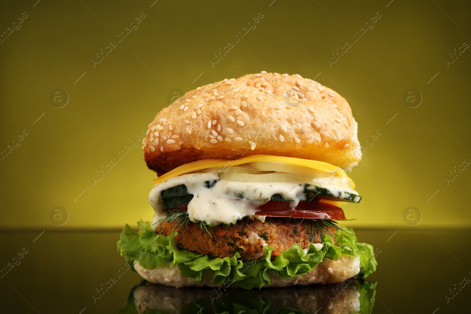 Photo of Delicious vegetarian burger on mirror surface against olive background