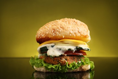 Photo of Delicious vegetarian burger on mirror surface against olive background