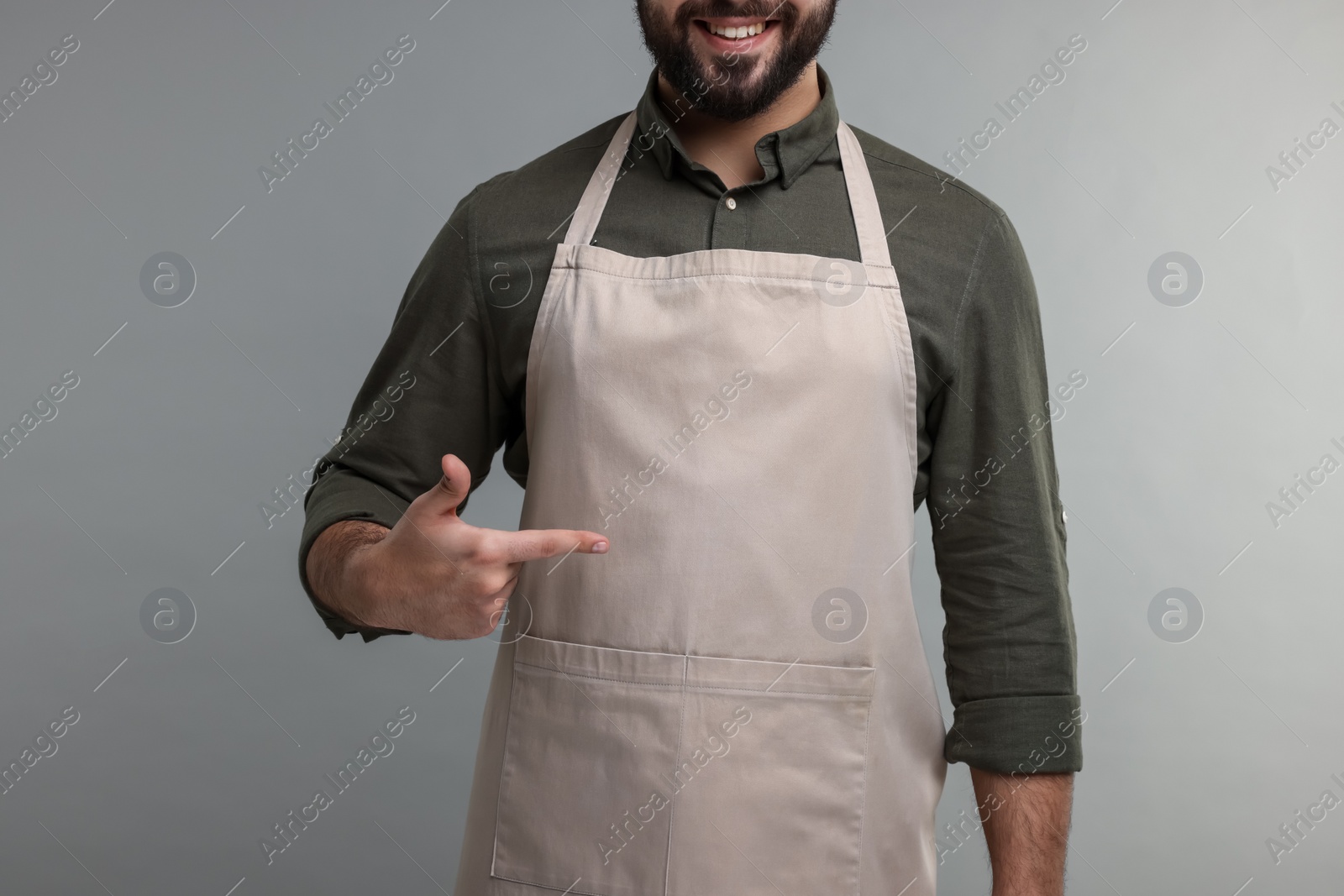 Photo of Smiling man pointing at kitchen apron on grey background, closeup. Mockup for design