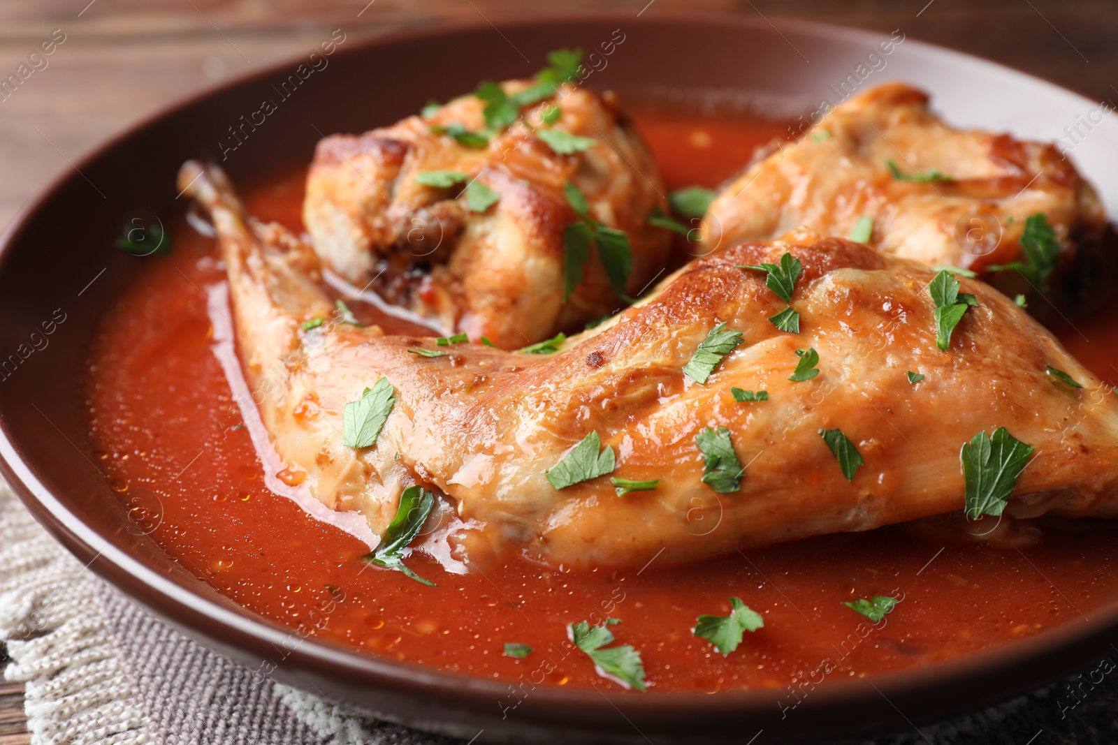 Photo of Tasty cooked rabbit meat with sauce and parsley on table, closeup