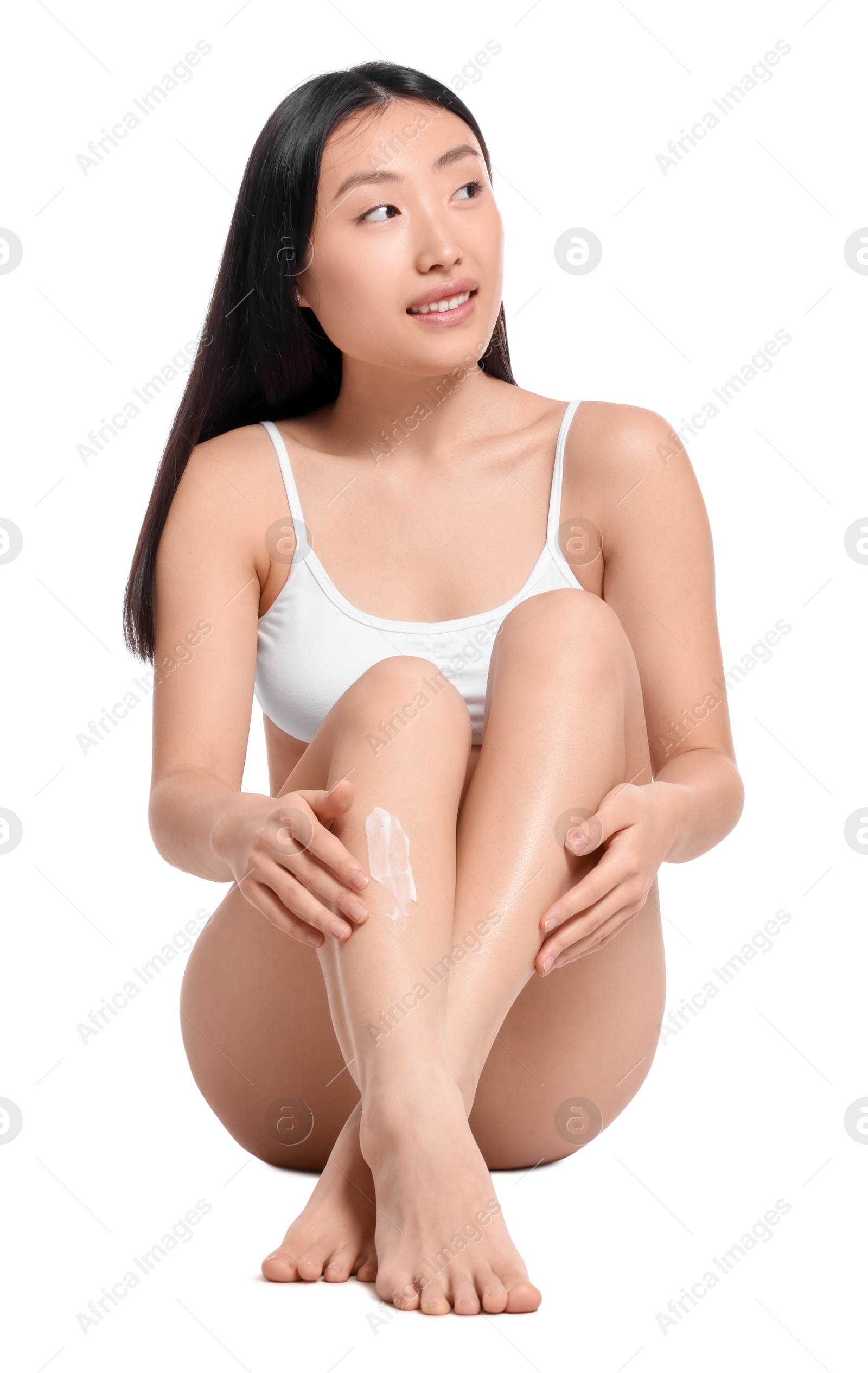 Photo of Beautiful young Asian woman applying body cream onto legs on white background
