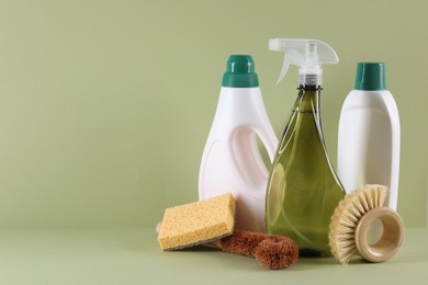 Bottles of cleaning product, brushes and sponge on light green background. Space for text