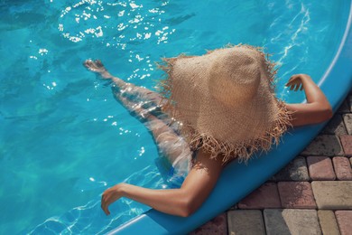 Photo of African American woman with straw hat resting in outdoor swimming pool on sunny summer day, above view