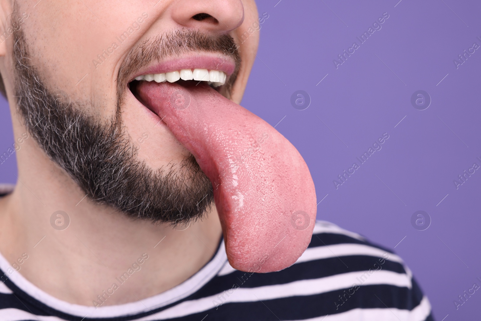 Image of Man showing long tongue on purple background, closeup