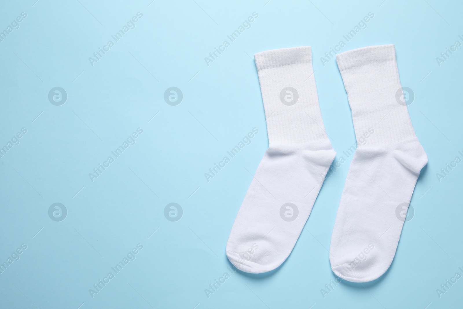 Photo of Pair of white socks on light blue background, flat lay. Space for text