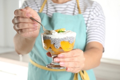 Photo of Woman eating tasty peach dessert with yogurt and chia seeds in kitchen, closeup