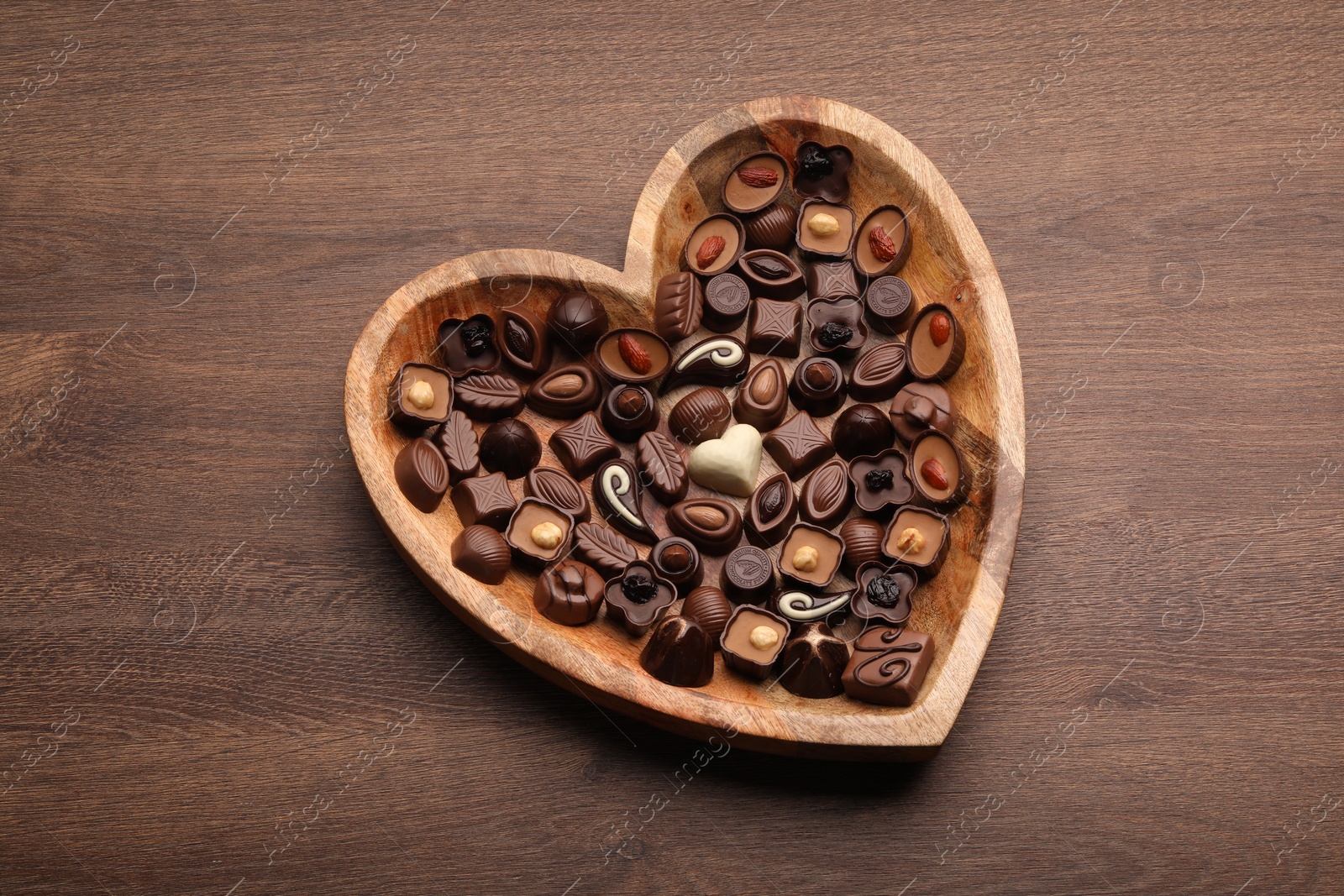Photo of Heart shaped plate with delicious chocolate candies on wooden table, top view