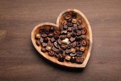 Heart shaped plate with delicious chocolate candies on wooden table, top view