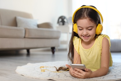 Cute child with headphones and mobile phone on floor indoors. Space for text