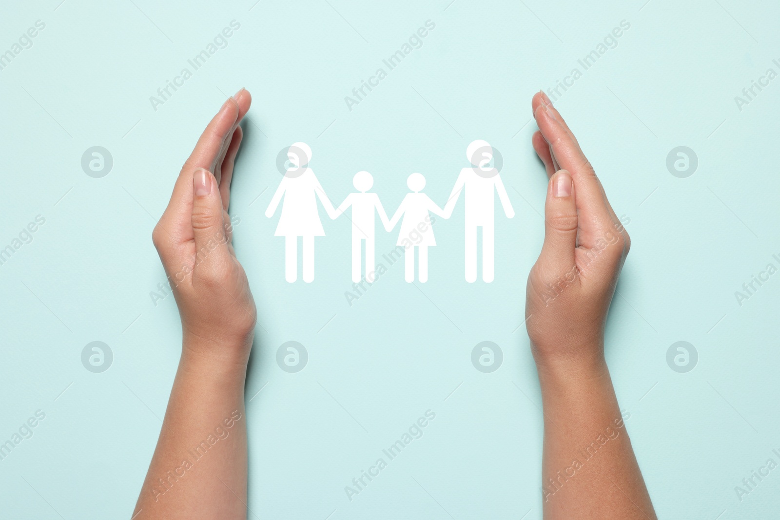 Image of Woman holding hands around paper silhouette of family on light blue background, top view. Insurance concept