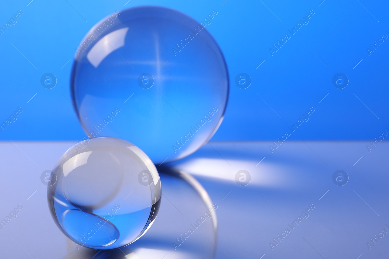 Photo of Transparent glass balls on mirror surface against blue background