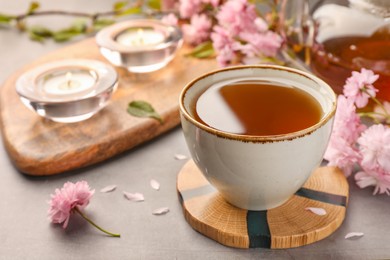 Photo of Traditional ceremony. Cup of brewed tea, teapot and sakura flowers on grey table, closeup