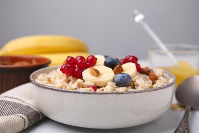 Oatmeal served with berries, almonds and banana slices on white table, closeup