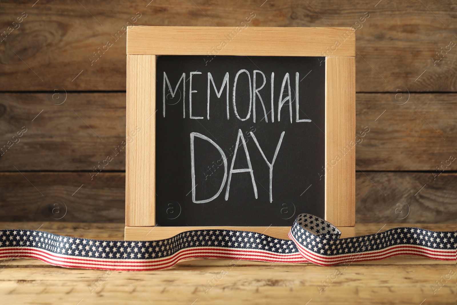 Photo of Blackboard with phrase Memorial Day and ribbon on wooden table