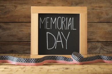 Photo of Blackboard with phrase Memorial Day and ribbon on wooden table