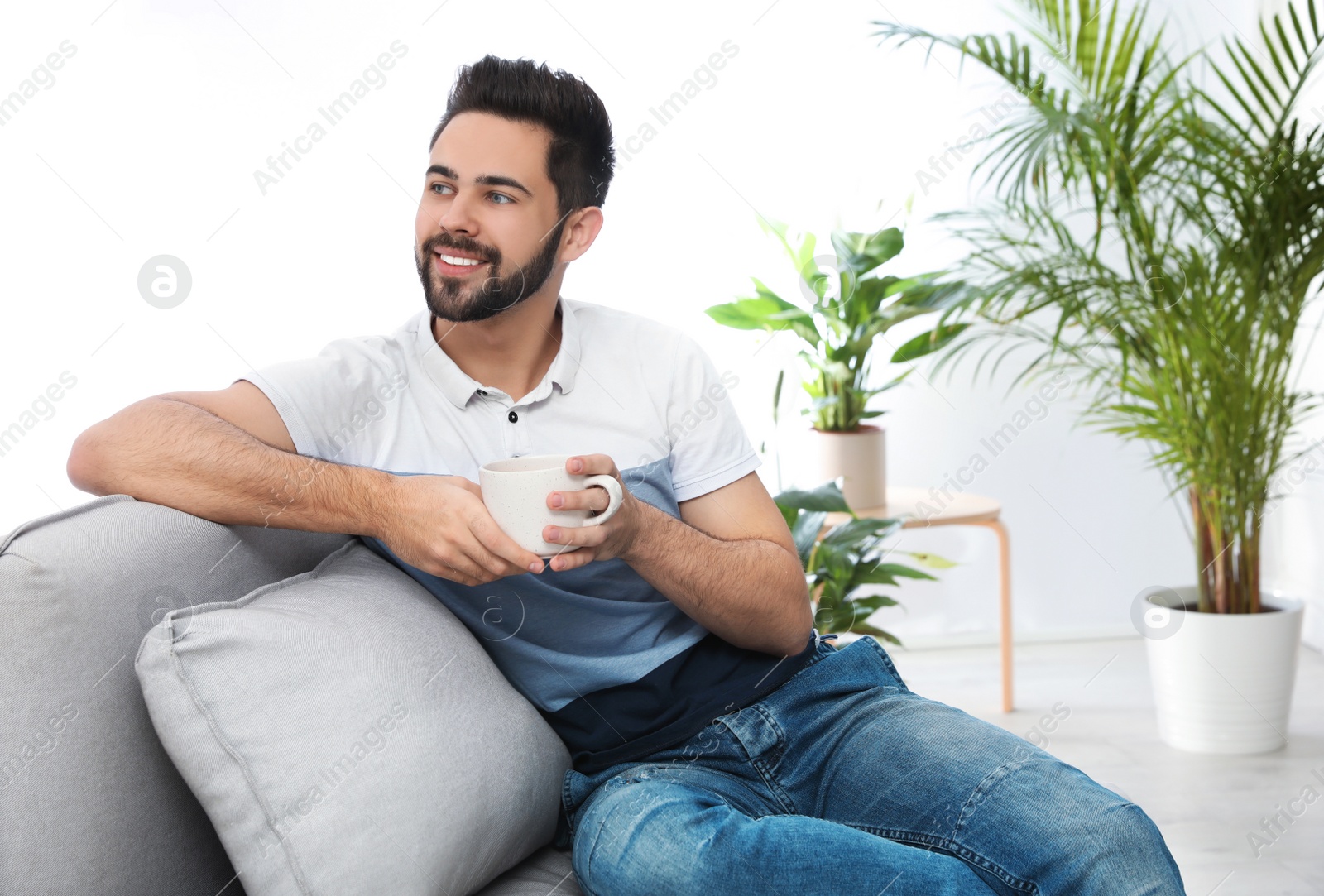 Photo of Young man with cup of drink relaxing on couch at home