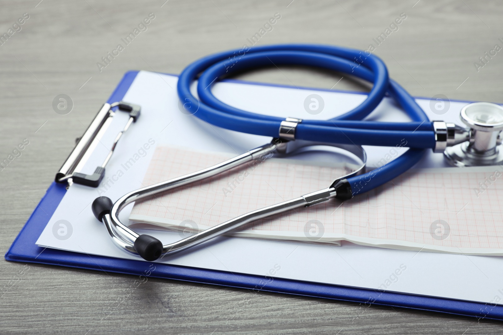 Photo of Clipboard with stethoscope and cardiogram on wooden table, closeup