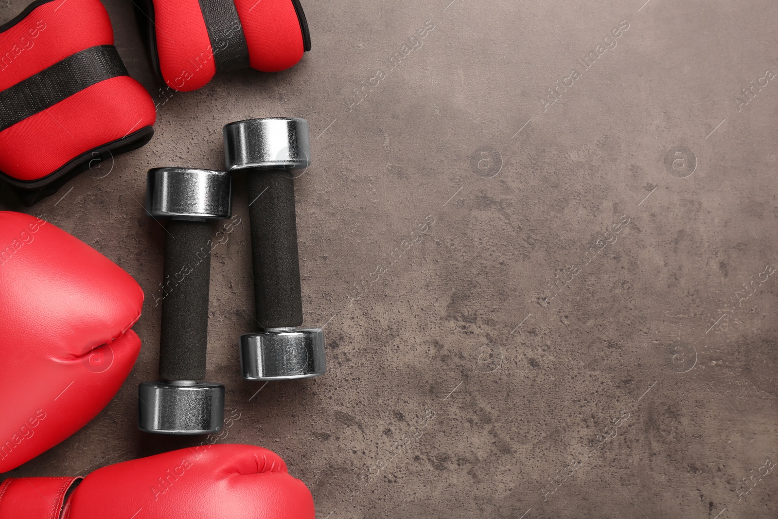 Photo of Metal dumbbells, boxing gloves and weights on brown textured table, flat lay. Space for text