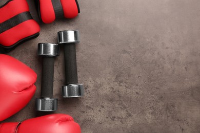 Photo of Metal dumbbells, boxing gloves and weights on brown textured table, flat lay. Space for text
