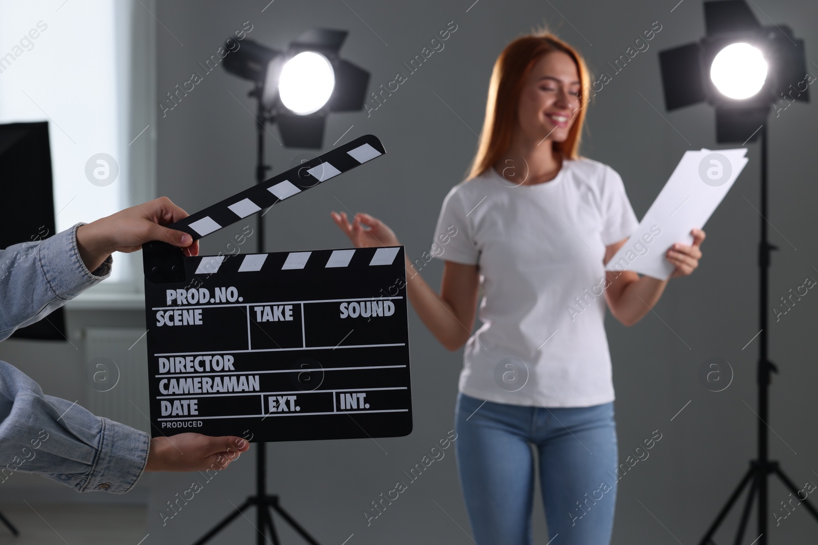 Photo of Casting call. Young woman performing while second assistance camera holding clapperboard against grey background in studio, selective focus