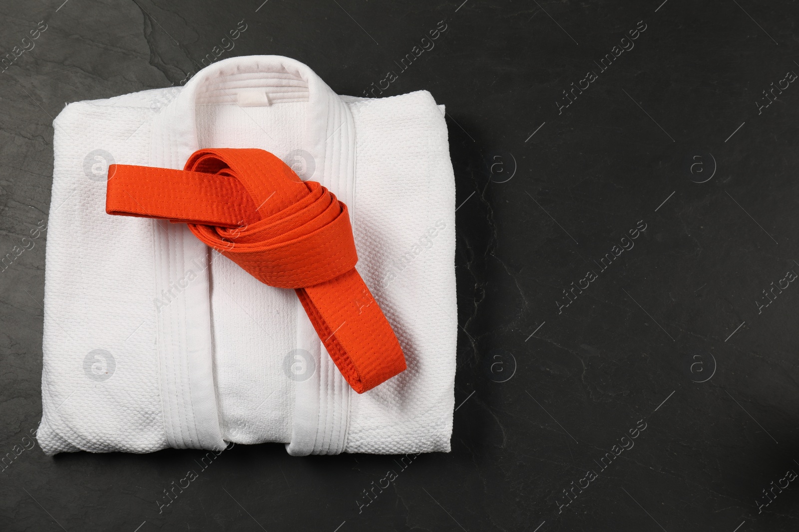 Photo of Orange karate belt and white kimono on gray background, top view. Space for text