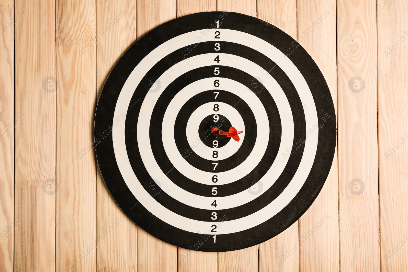 Photo of Dart board with color arrow on wooden background, top view