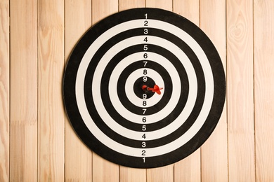 Photo of Dart board with color arrow on wooden background, top view