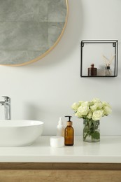 Photo of Beautiful roses and bath accessories near sink in bathroom