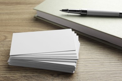 Stack of blank business cards, notebook and pen on wooden table. Mockup for design