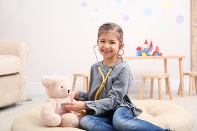 Cute child playing doctor with stuffed toy on floor in hospital