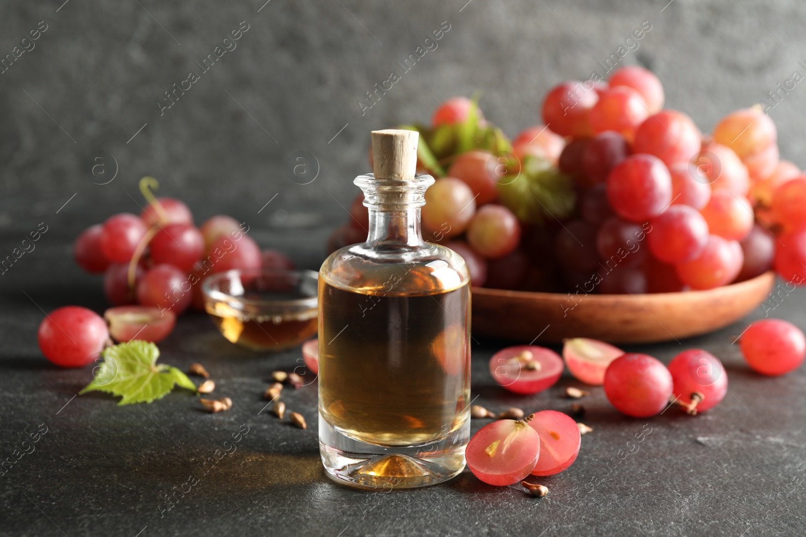 Photo of Organic red grapes, seeds and bottle of natural essential oil on black table