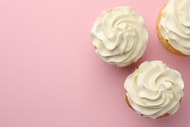 Tasty vanilla cupcakes with cream on pink background, flat lay. Space for text