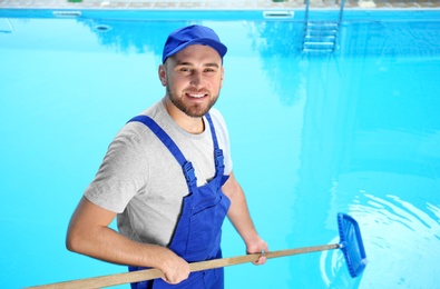 Male worker cleaning outdoor pool with scoop net