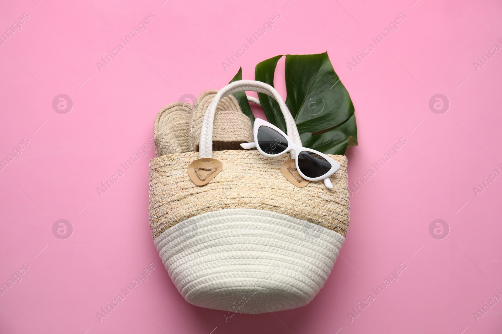 Photo of Elegant woman's straw bag with shoes, tropical leaf and sunglasses on pink background, top view